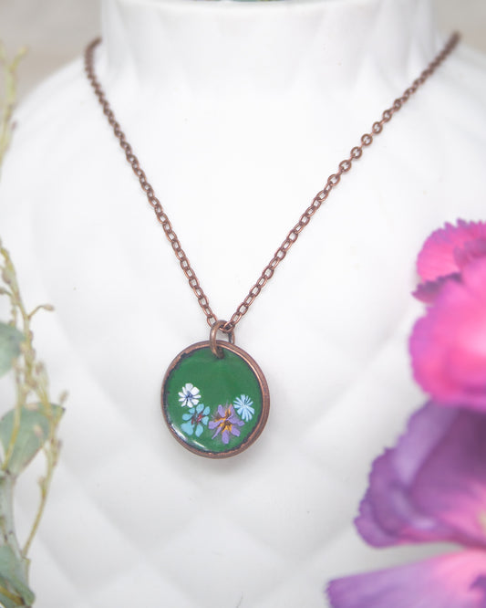 A necklace with a green pendant featuring colorful flowers is displayed against a white background.