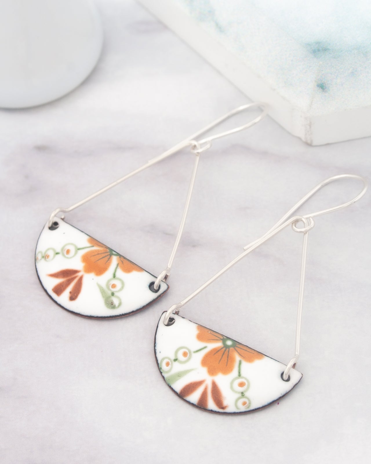 A pair of white earrings with a floral design hangs from a hook on a marble surface.