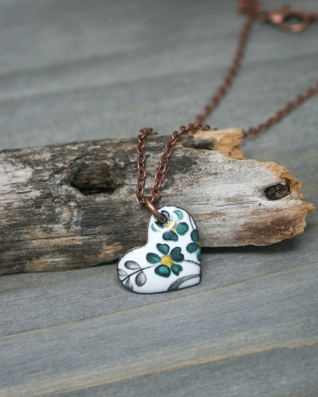 a white and green heart shaped pendant on a brown chain