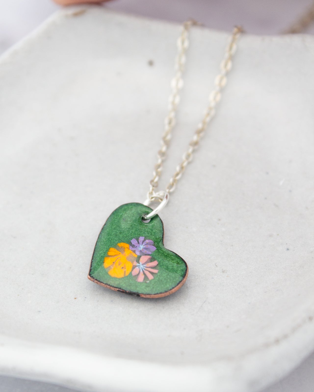 A green heart-shaped pendant with colorful flowers is displayed on a white surface.