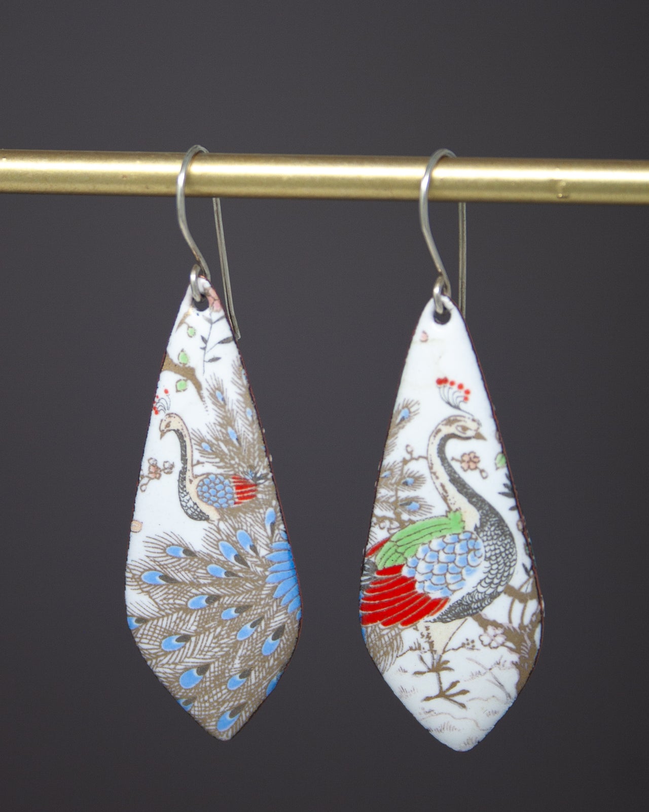 A pair of earrings with a decorative design featuring a peacock and other colorful elements.