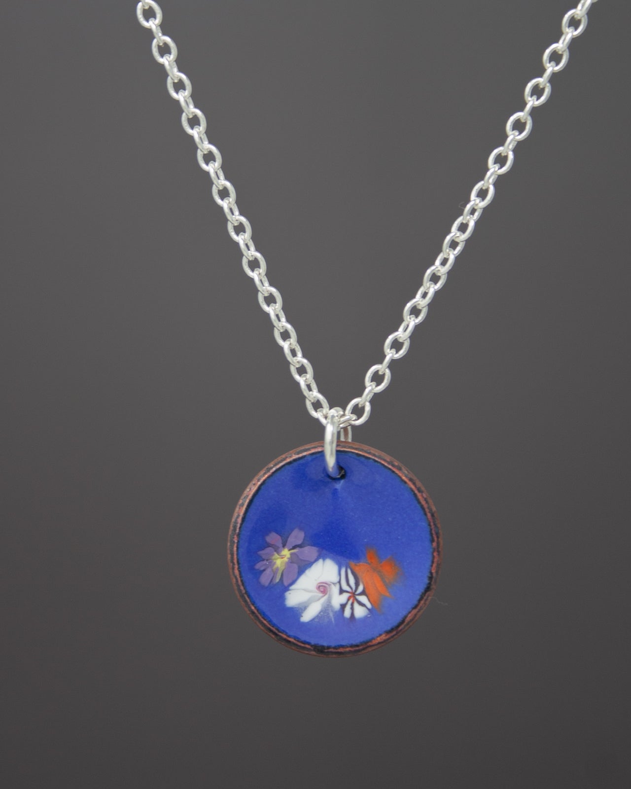 A necklace with a circular pendant featuring a floral design in blue, orange, and white colors.