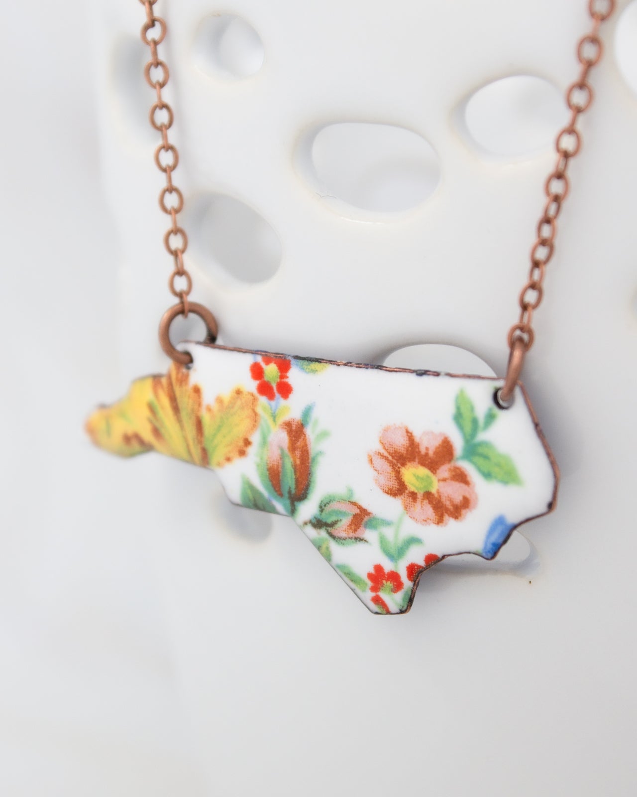 A necklace with a pendant in the shape of the state of North Carolina, featuring a floral design.