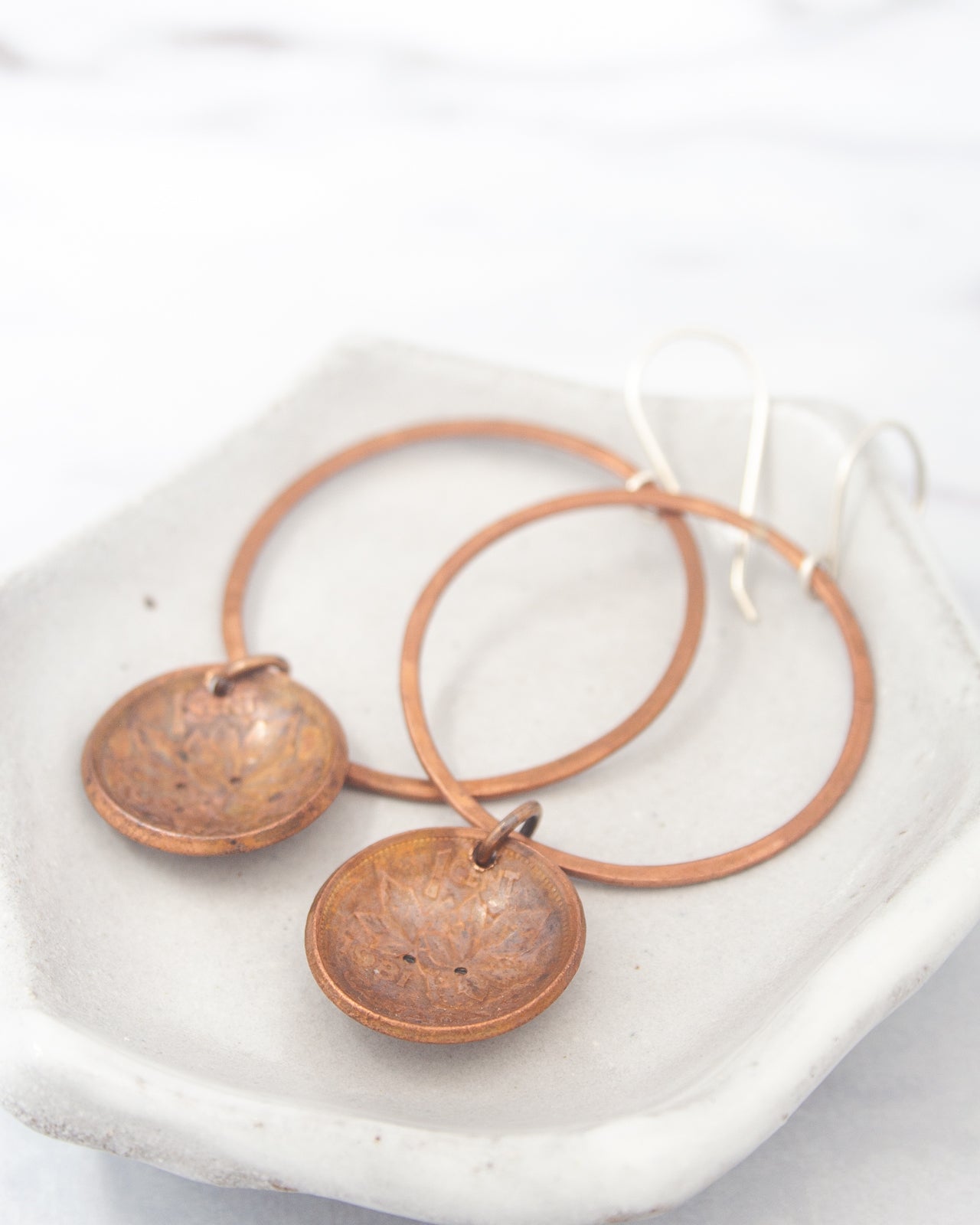 A pair of copper-colored earrings with circular pendants, resting on a white surface.