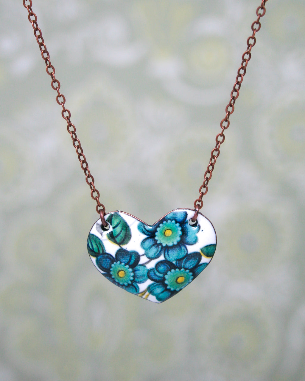 a heart shaped necklace with blue flowers on a chain