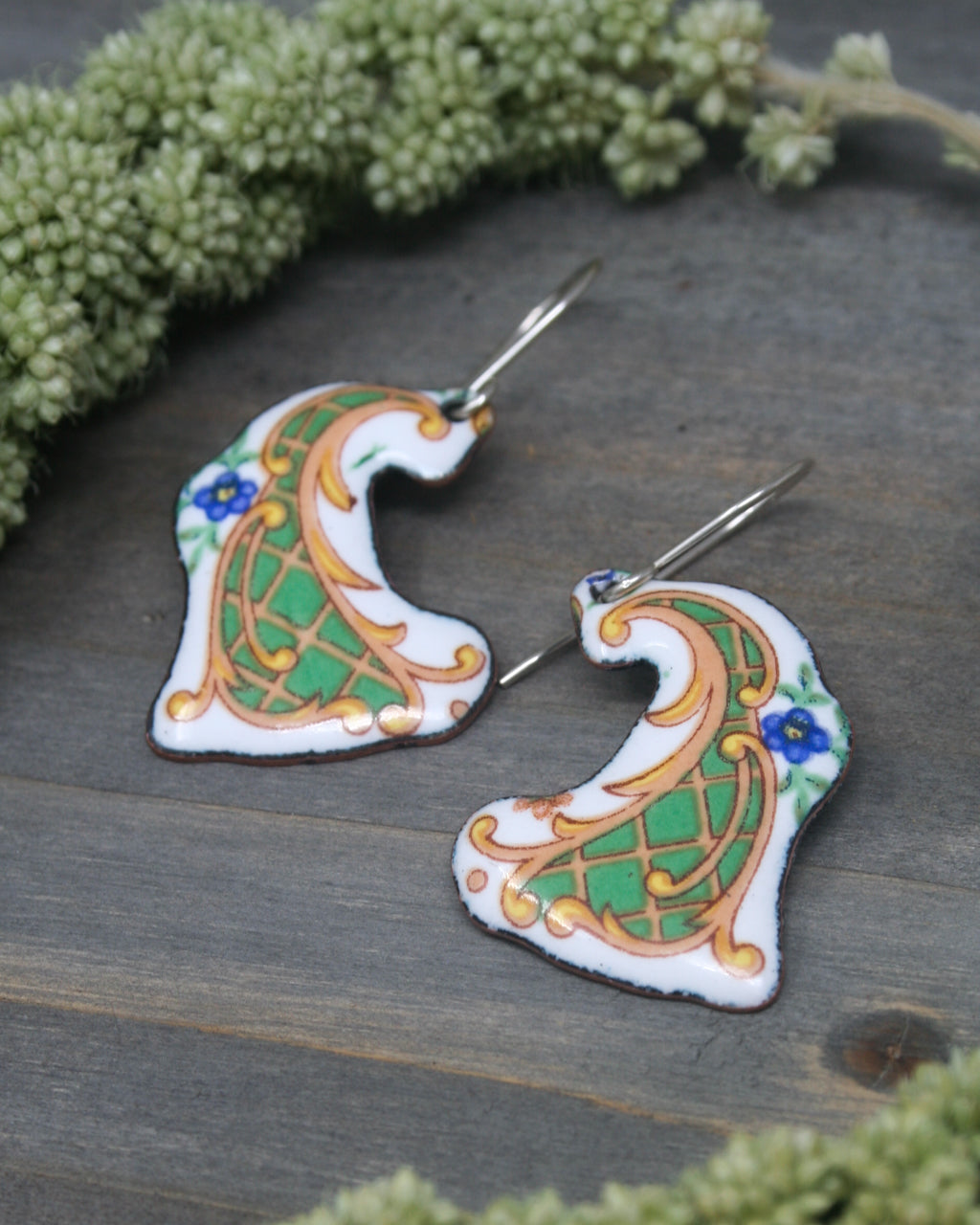 two ornate earrings with intricate designs, placed on a wooden surface.