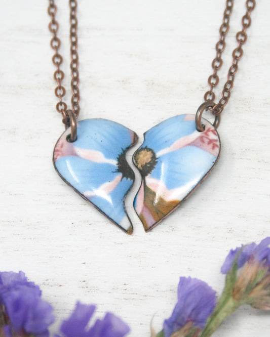 A heart-shaped pendant necklace with two blue flower-shaped pendants, one larger and one smaller, connected by a chain.