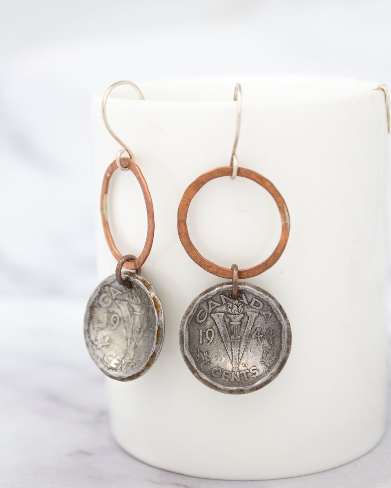 a pair of earrings with a combination of copper and silver materials, including a circular pendant and a dangling hook.