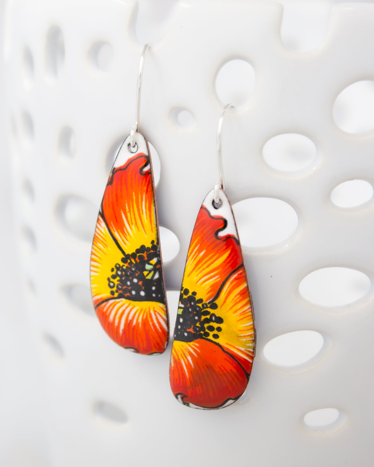 A pair of earrings with a vibrant, colorful design featuring a large orange and yellow flower-like shape.