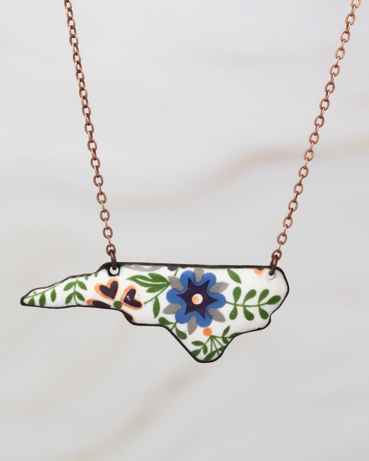 A necklace with a pendant in the shape of the state of North Carolina, featuring a floral design.