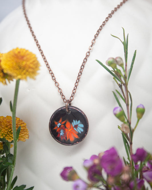 a necklace with a circular pendant, adorned with a floral design, surrounded by a variety of colorful flowers and plants.