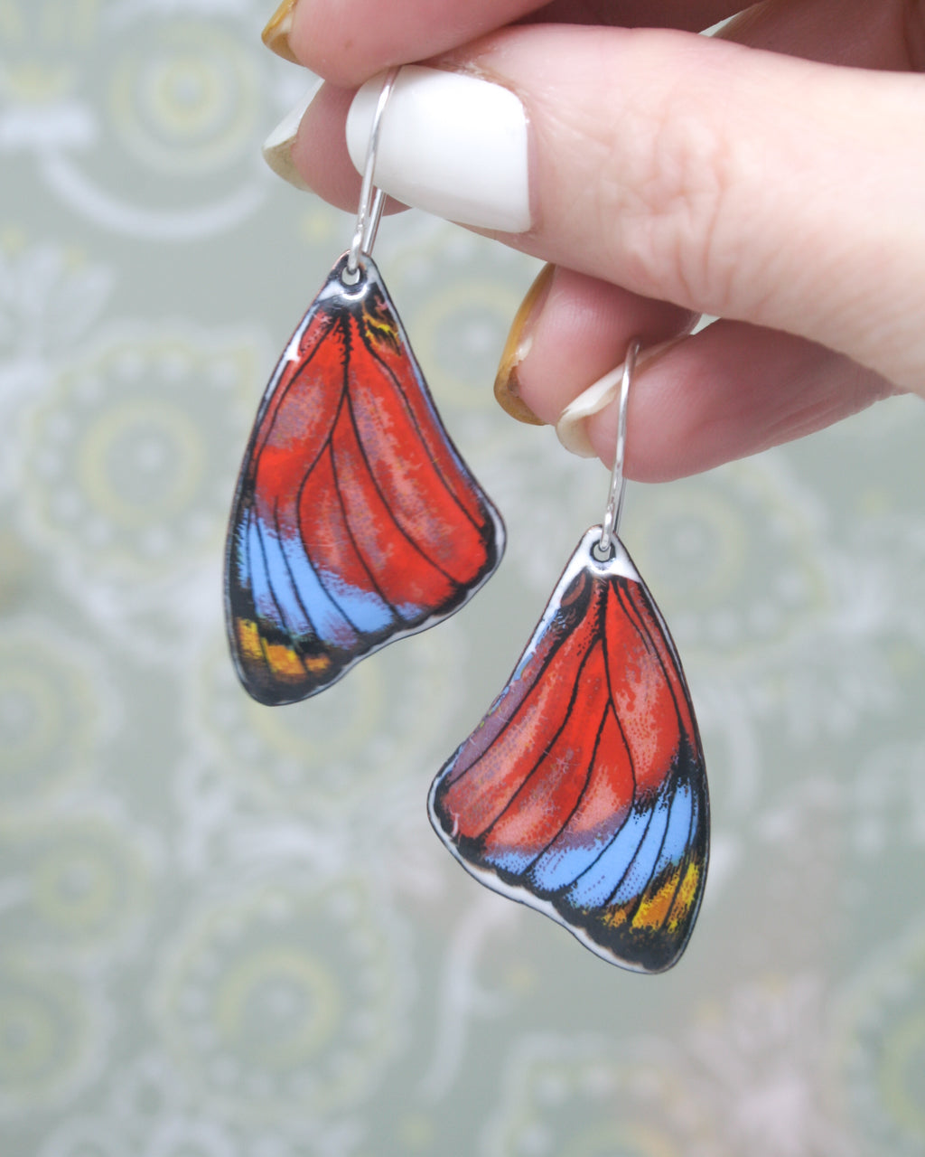 a woman's hand holding a pair of colorful butterfly earrings