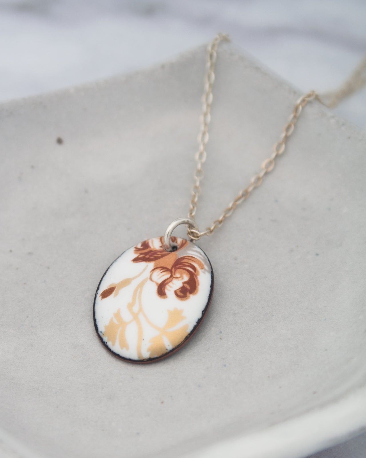 A necklace with a pendant featuring a floral design in brown and white colors.