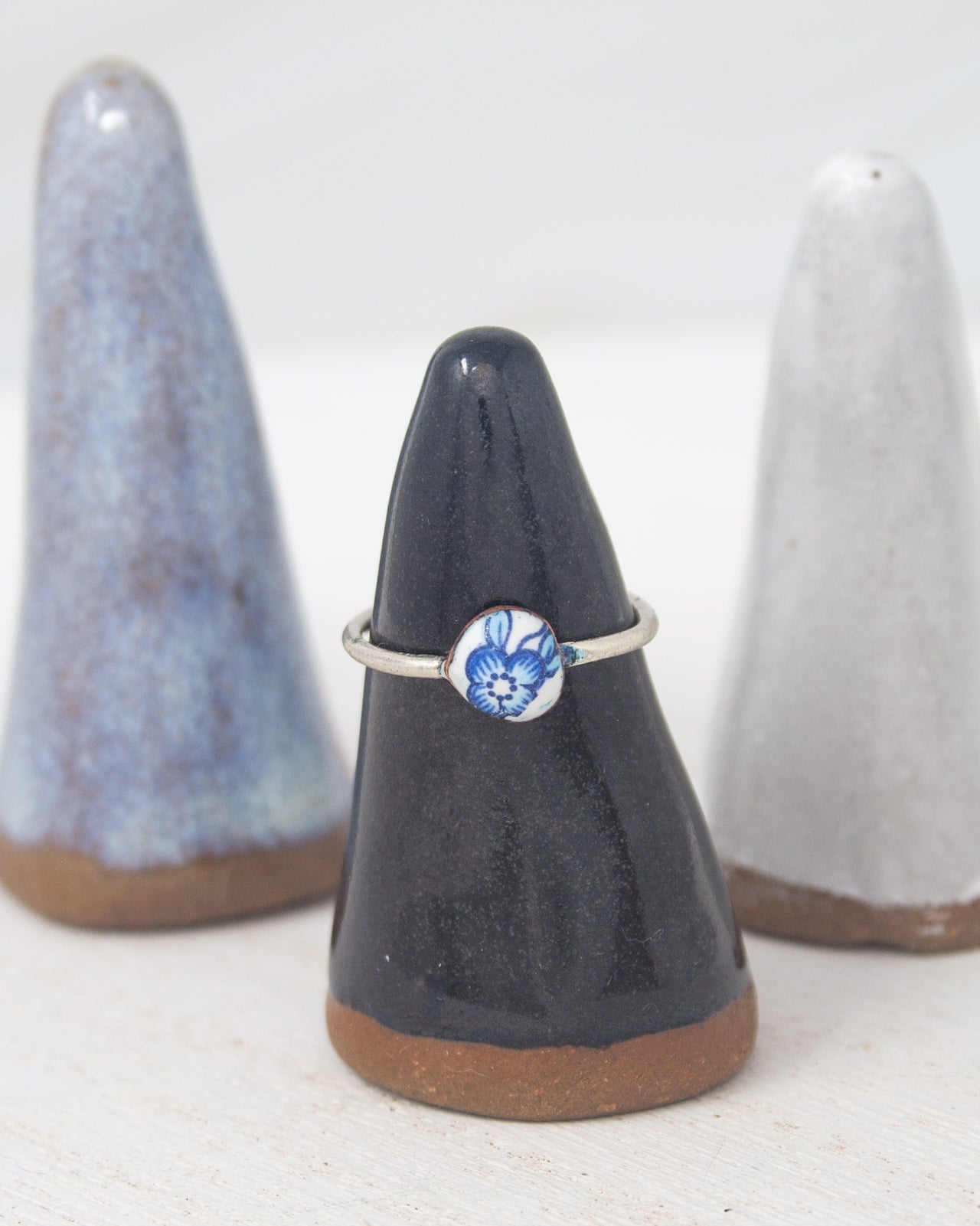 A black ceramic ring stand holding a silver ring with a blue floral design, placed between two white ceramic pinnacles.