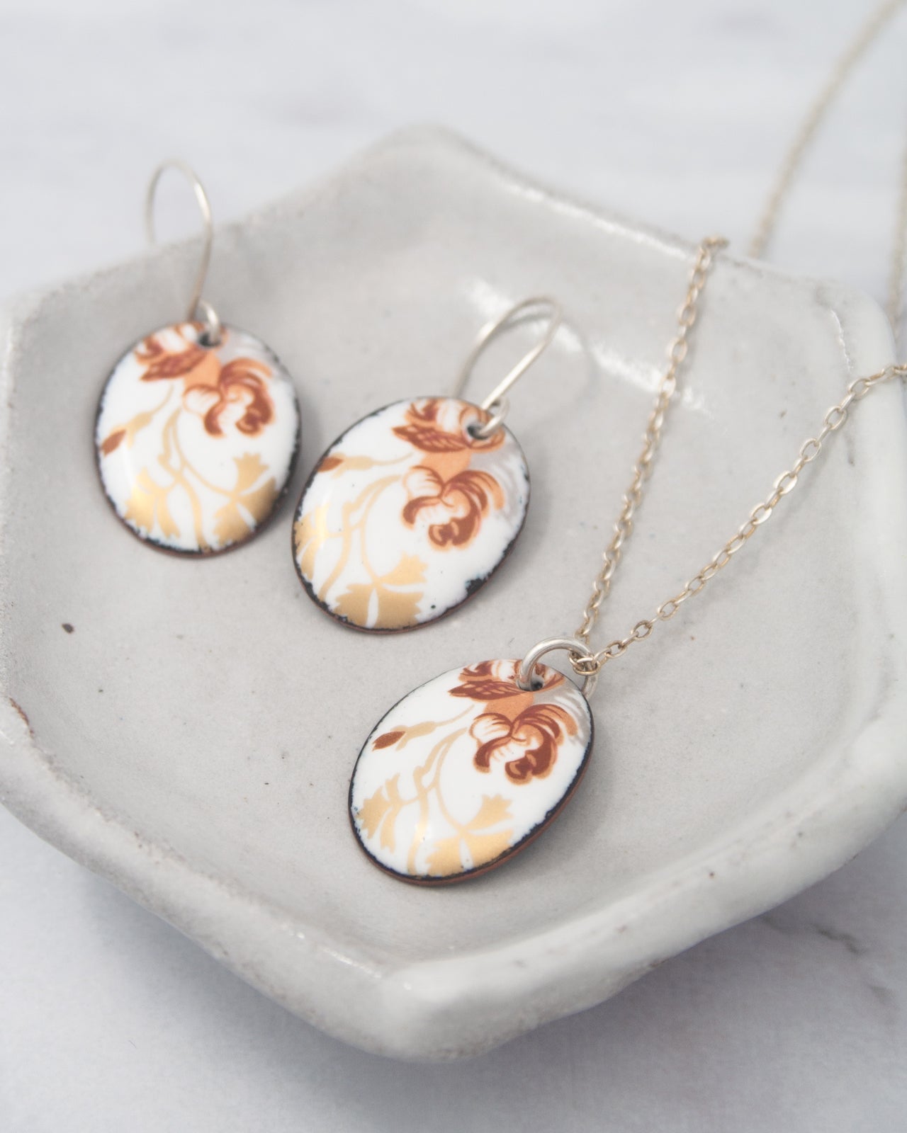 A pair of earrings and a necklace are displayed on a white plate, with the earrings featuring a floral design and the necklace having a chain.