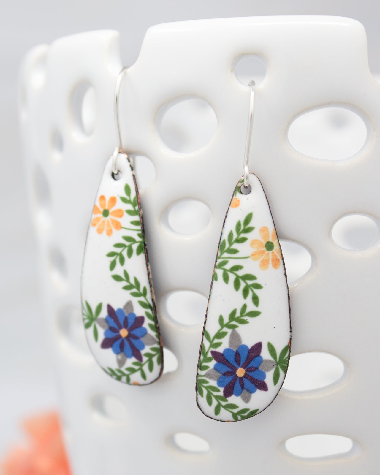 A pair of white earrings with colorful floral designs, hanging from a hook.