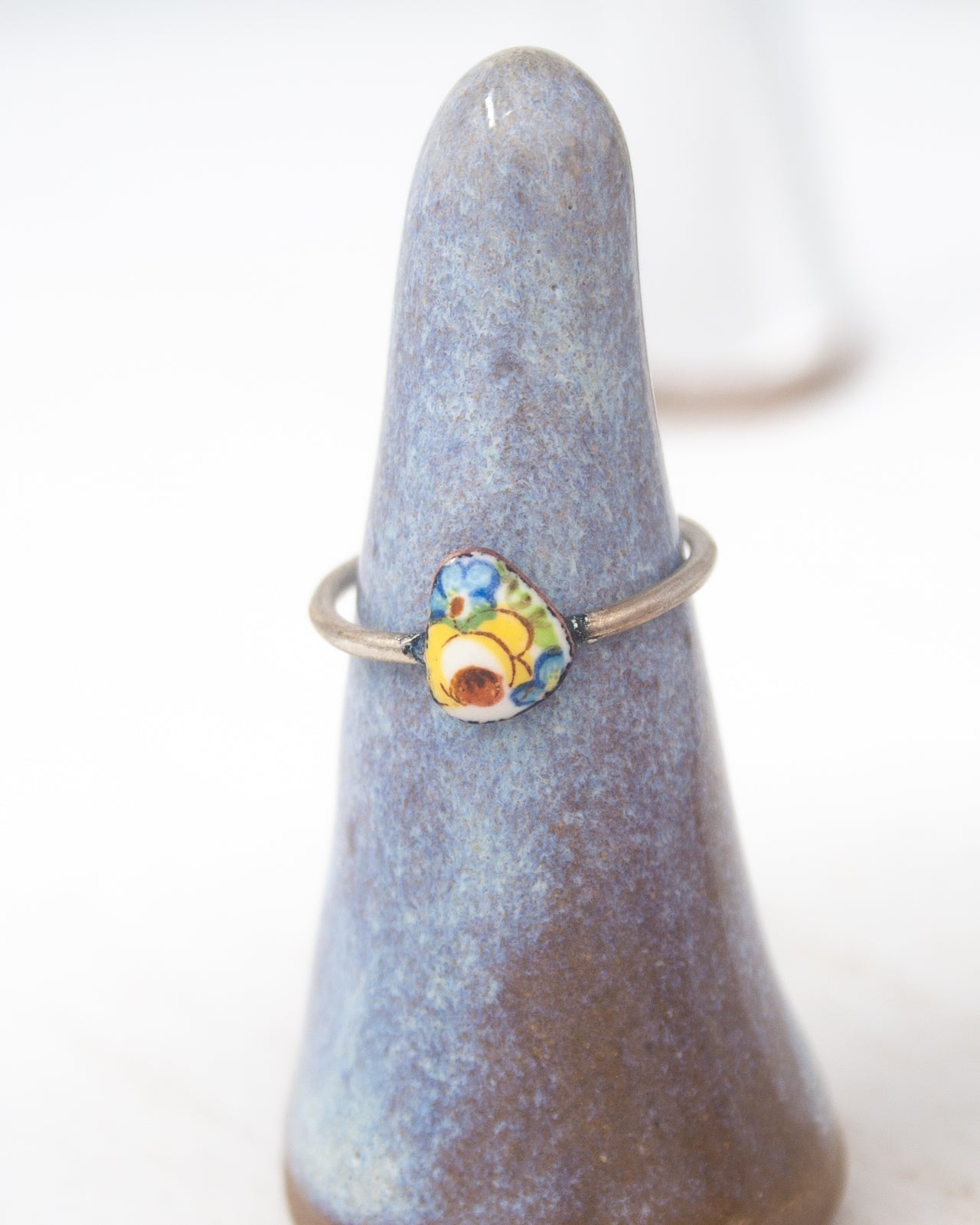 A ring with a colorful stone or gemstone is displayed on a blue ceramic stand.