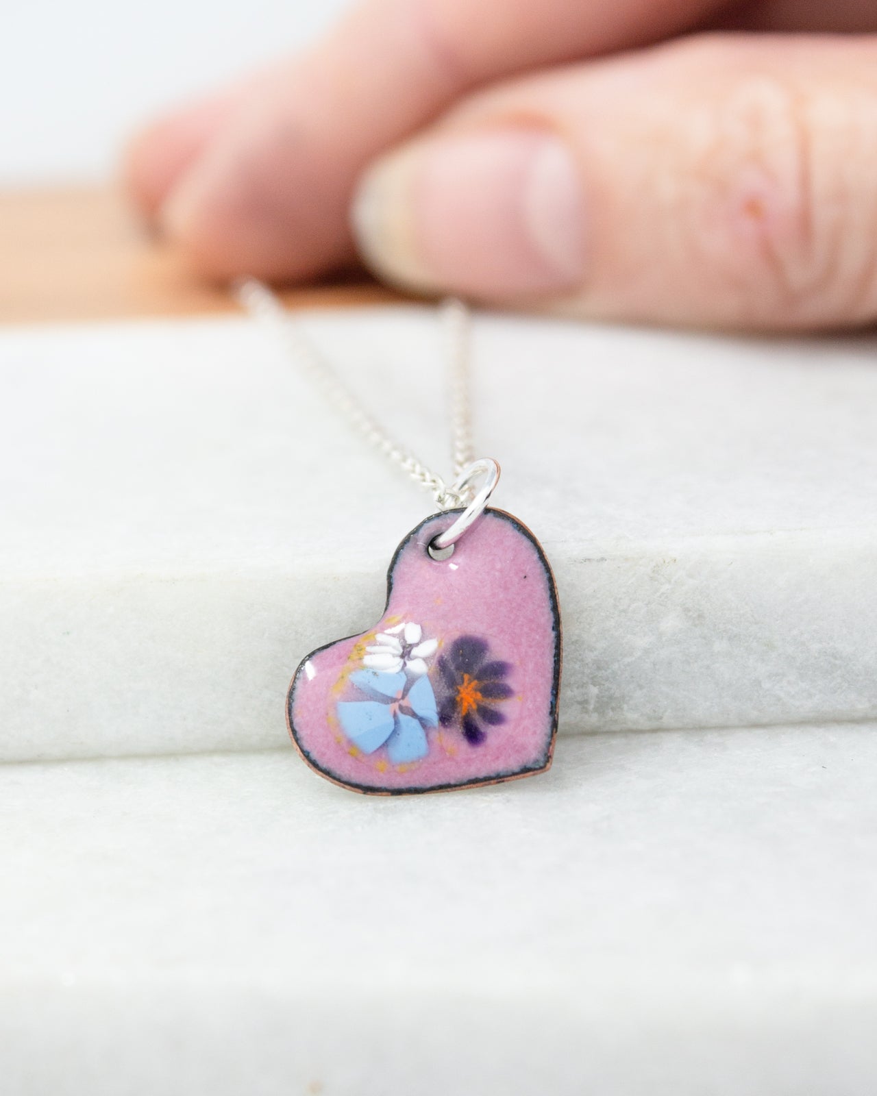 A hand is holding a heart-shaped pendant necklace with a floral design.