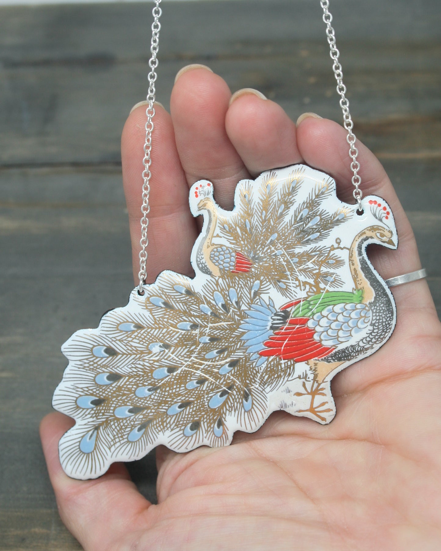 a person holding a peacock shaped pendant in their hand