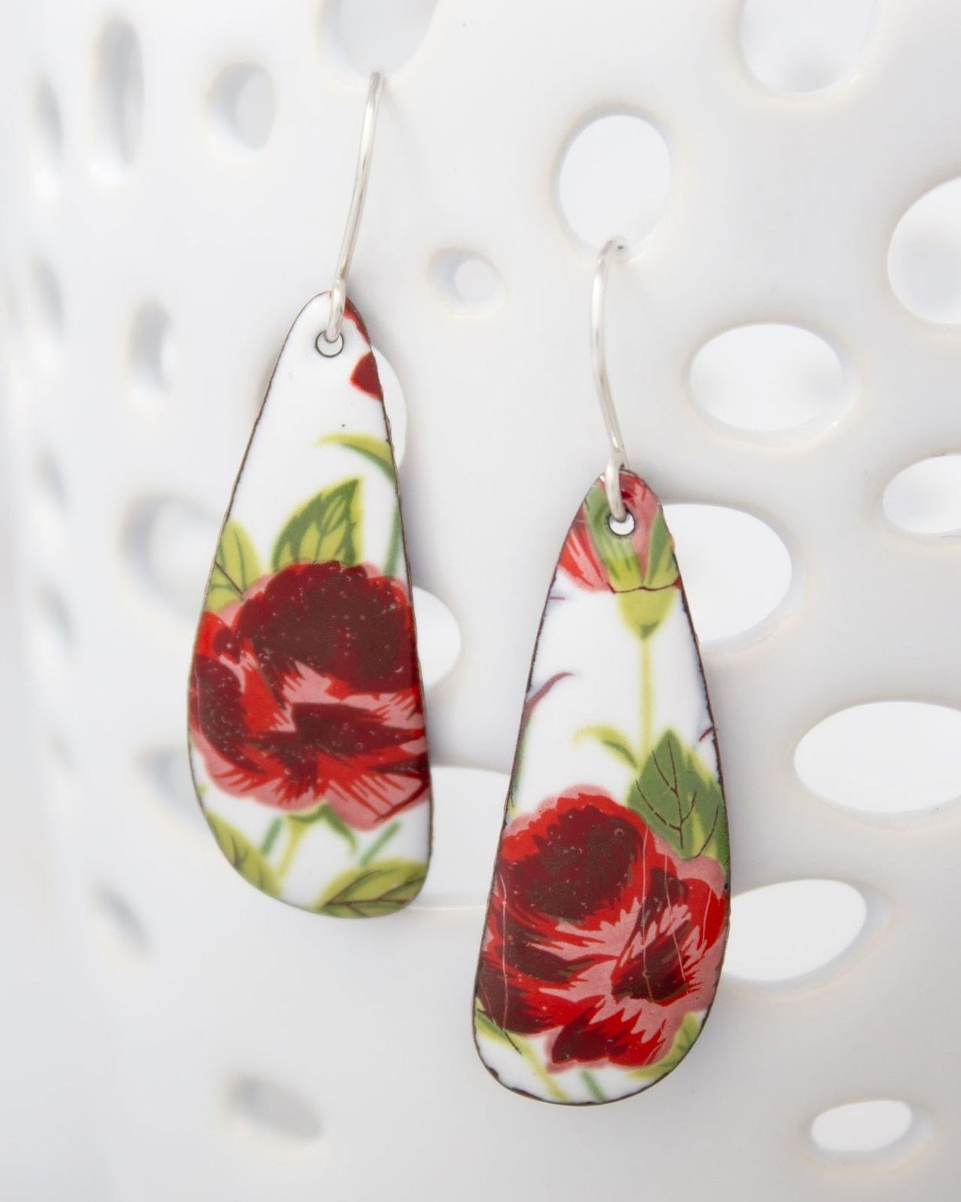 A pair of earrings with a floral design, featuring red and green flowers against a white background.