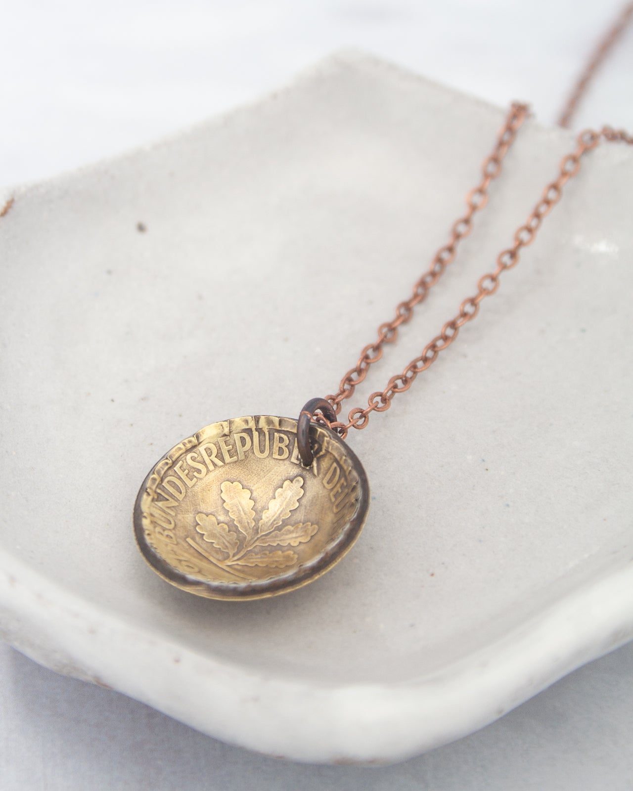A necklace with a pendant in the shape of a coin, resting on a white surface.