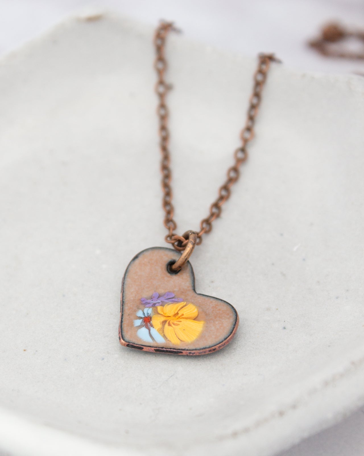 A heart-shaped pendant necklace with a floral design on it, resting on a white surface.