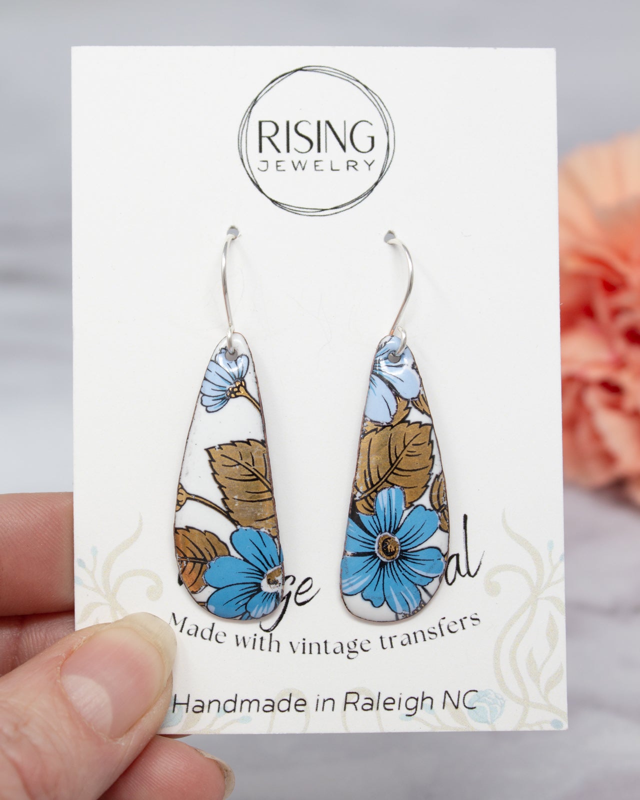 A hand holding a pair of earrings with a floral design, as part of a jewelry product.