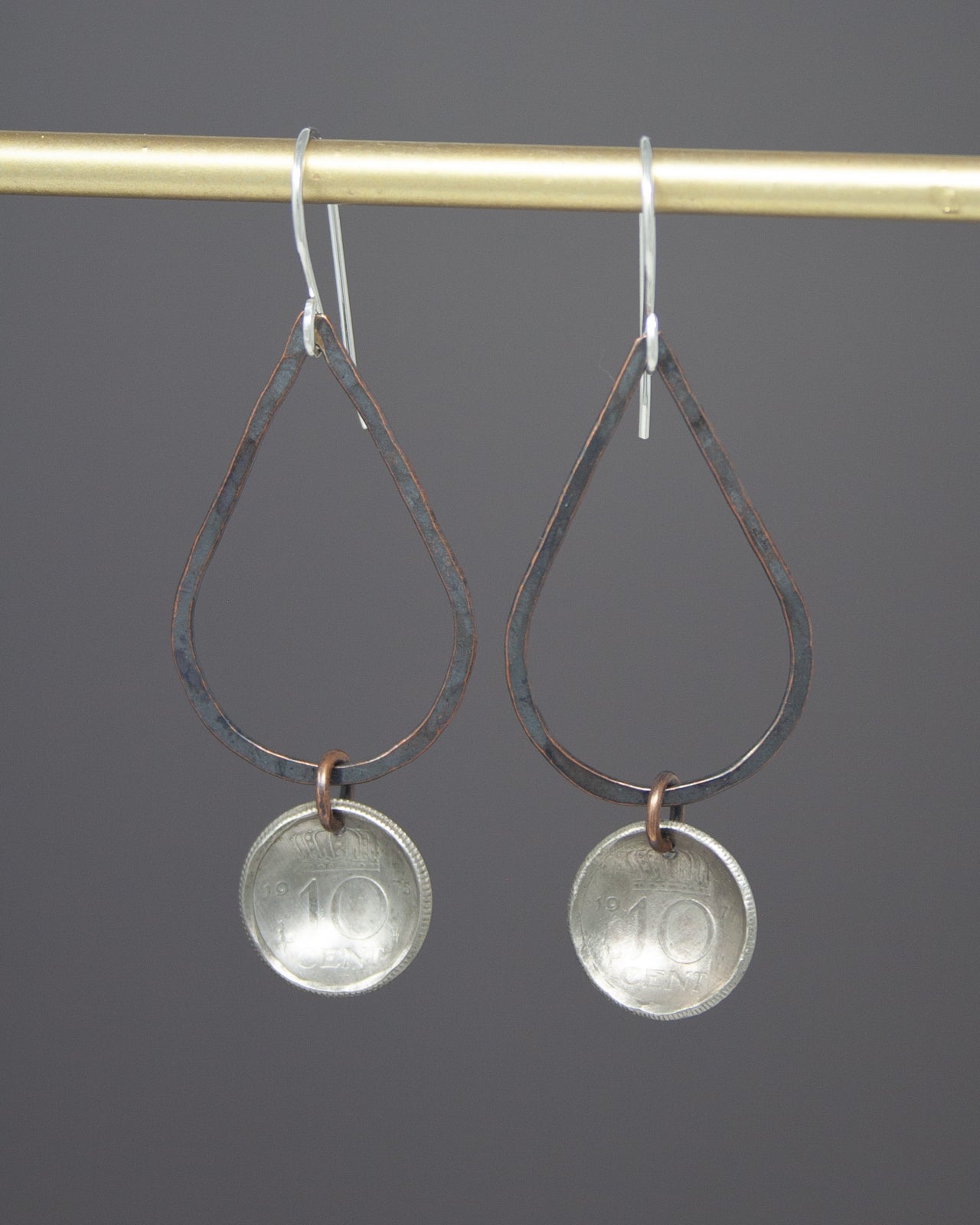 A pair of earrings with a metal frame and a metal coin charm hanging from a hook.