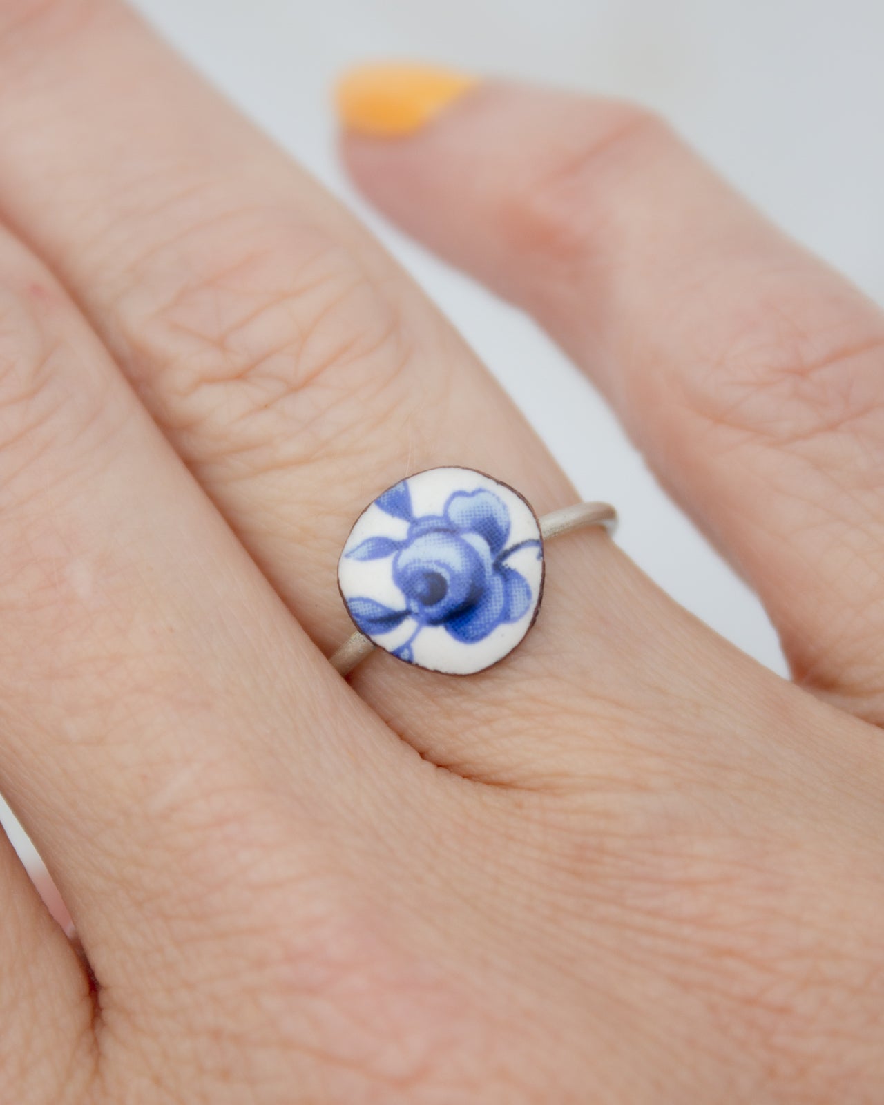 A close-up of a person's hand wearing a ring with a blue and white floral design.
