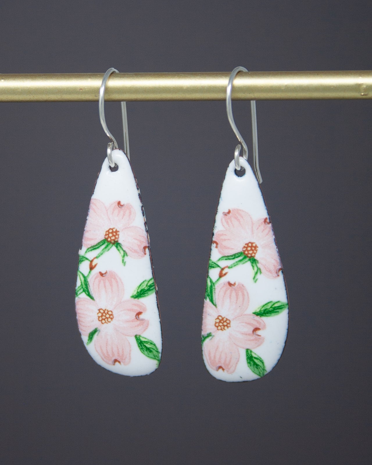 A pair of white earrings with pink flowers on a gold bar.