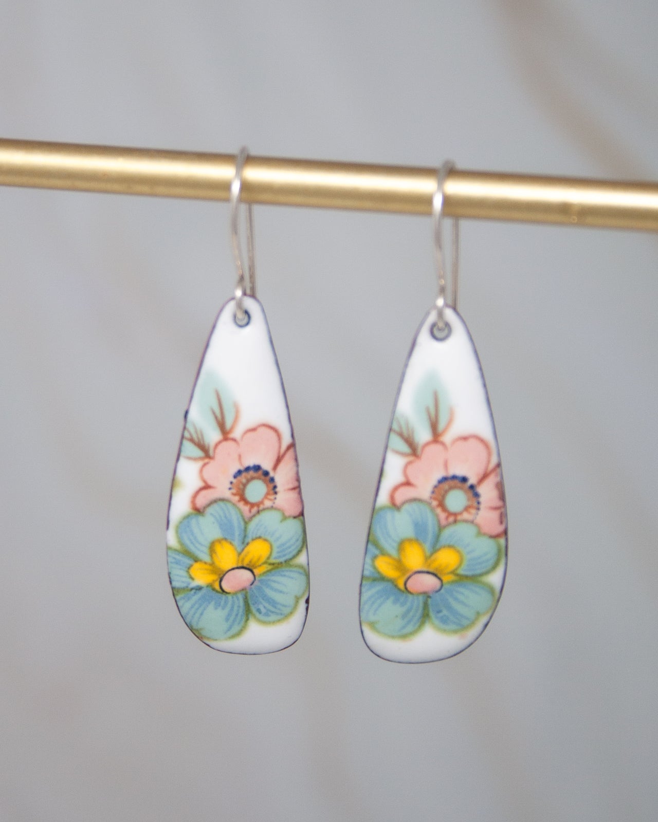 A pair of earrings with colorful floral designs on them, hanging from a gold bar.