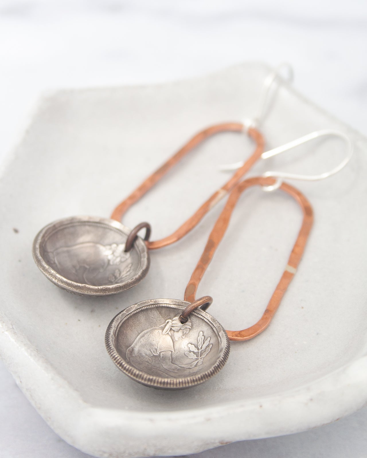 A pair of earrings with a silver-colored metal design and copper-colored metal accents, resting on a white surface.