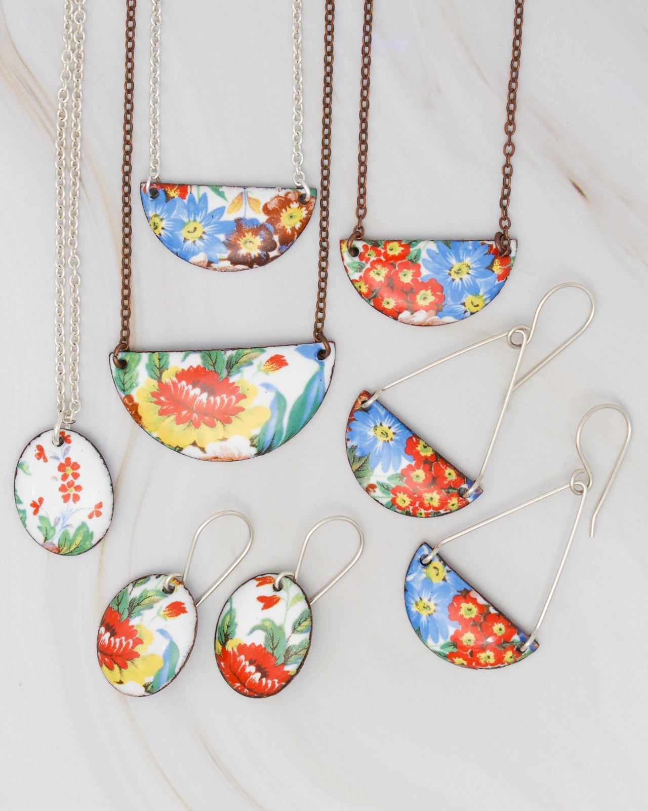 a collection of colorful floral-patterned jewelry, including necklaces and earrings, arranged on a marble surface.