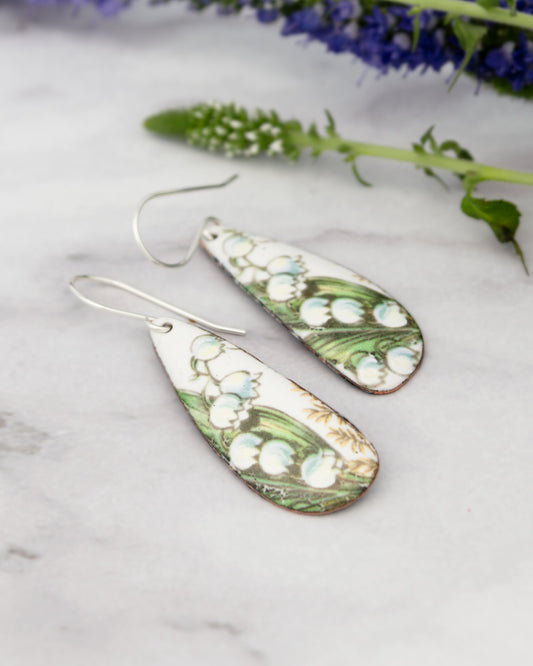 A pair of white earrings with a floral design, resting on a marble surface.