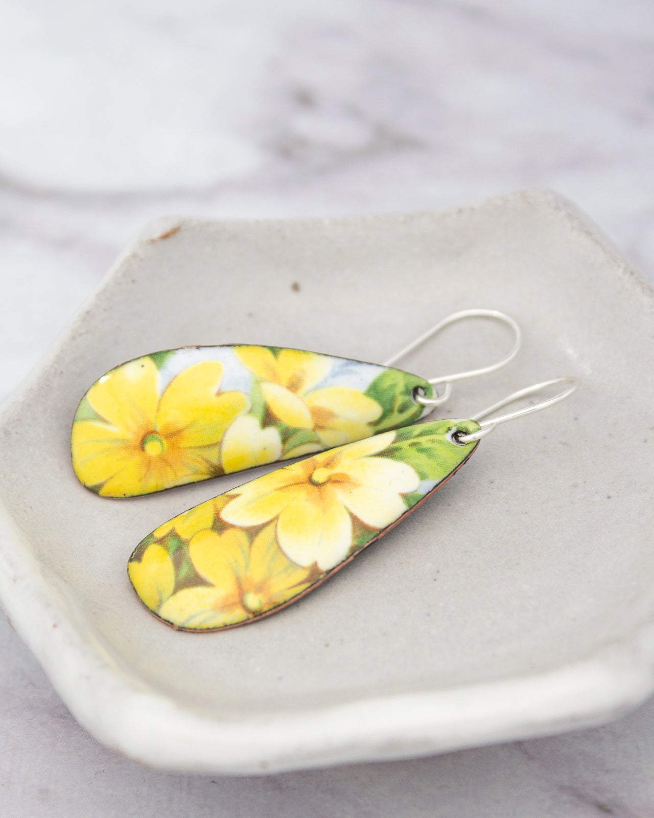 A pair of earrings with yellow flower designs on them, resting on a white plate or bowl.