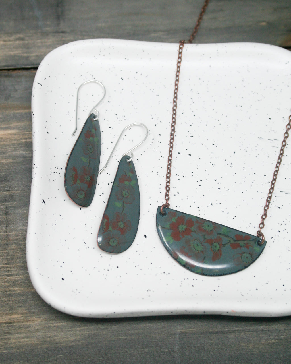 A pair of earrings and a necklace are displayed on a white plate with a speckled surface.