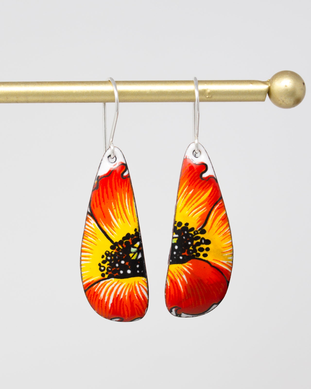 A pair of earrings with a vibrant floral design, featuring red and yellow petals with black centers.