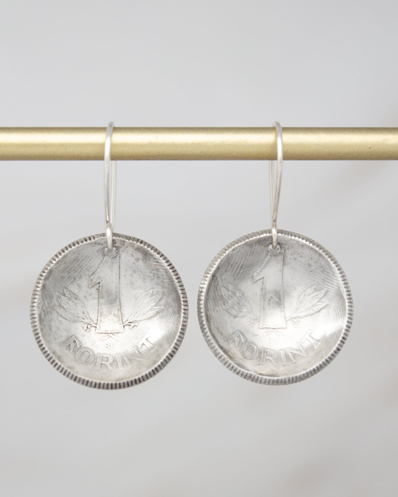 A pair of silver earrings shaped like a one-cent coin, with the word "NORINT" engraved on them.