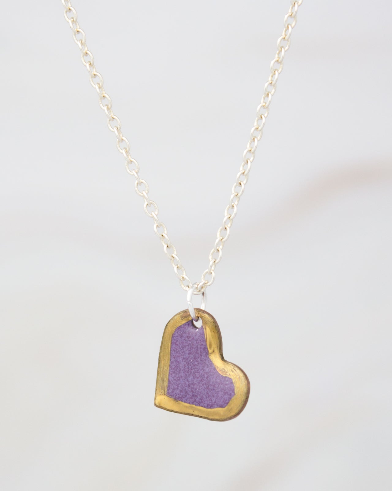 A delicate necklace with a heart-shaped pendant in a vibrant purple color, suspended from a chain.