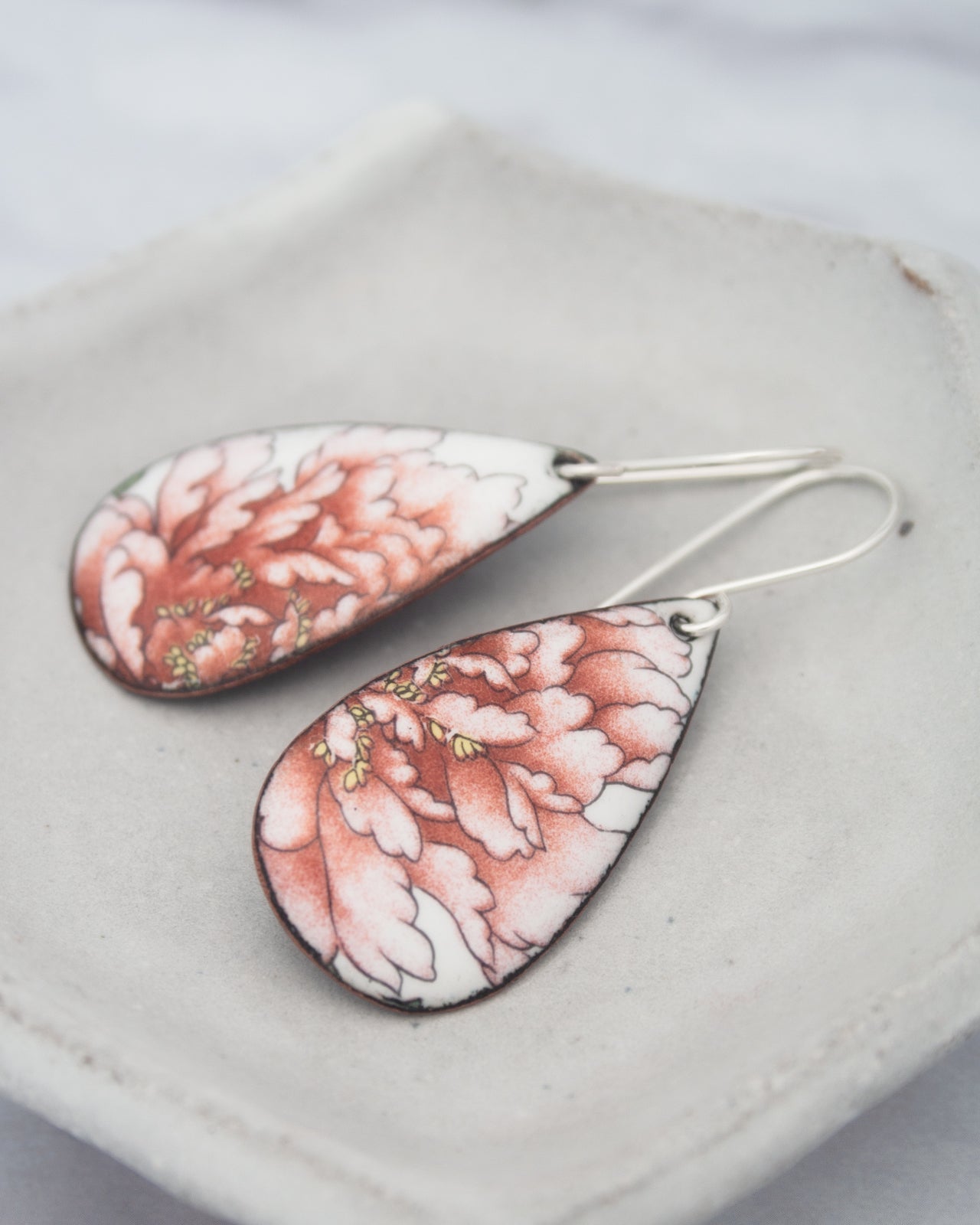 A pair of earrings with a floral design, featuring red and white colors.