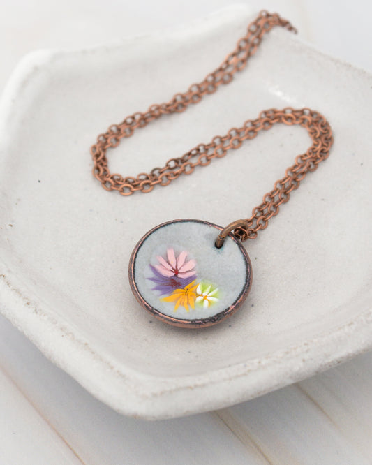 A necklace with a circular pendant featuring a floral design is displayed on a white plate.