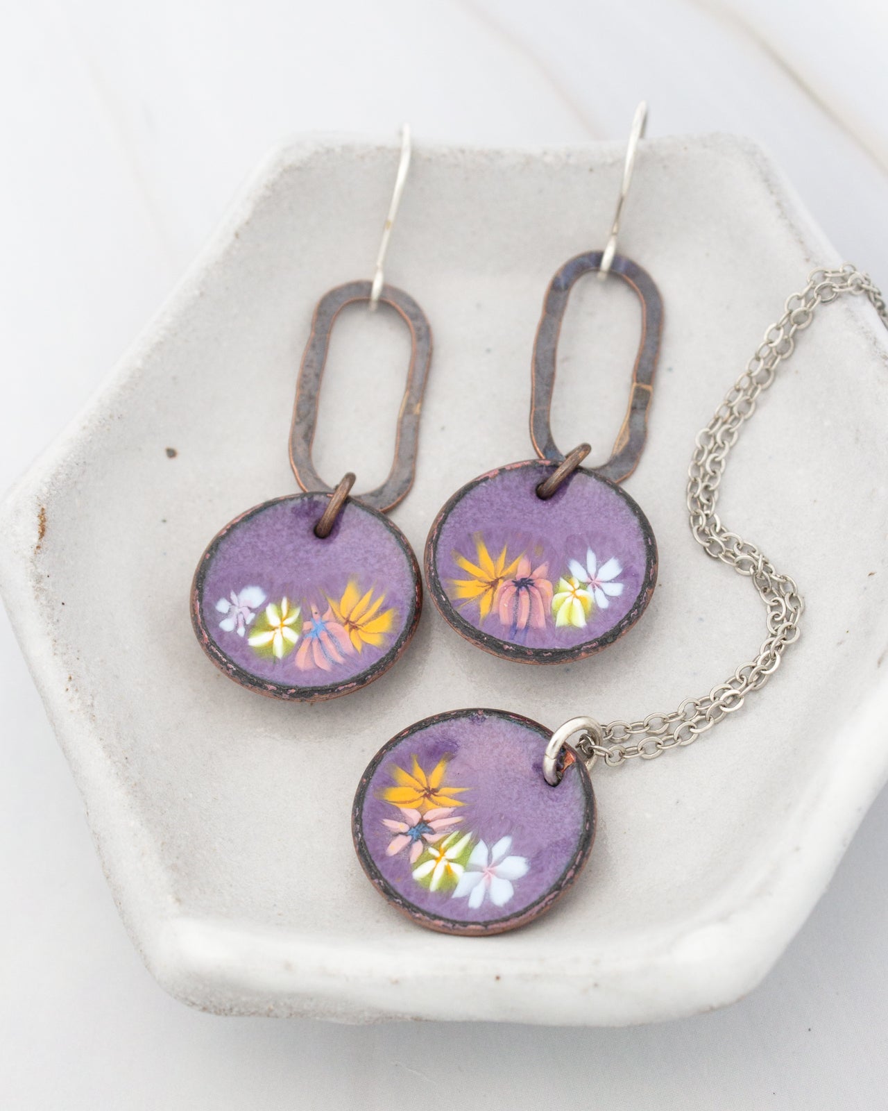 A pair of purple earrings and a necklace are displayed on a white plate.