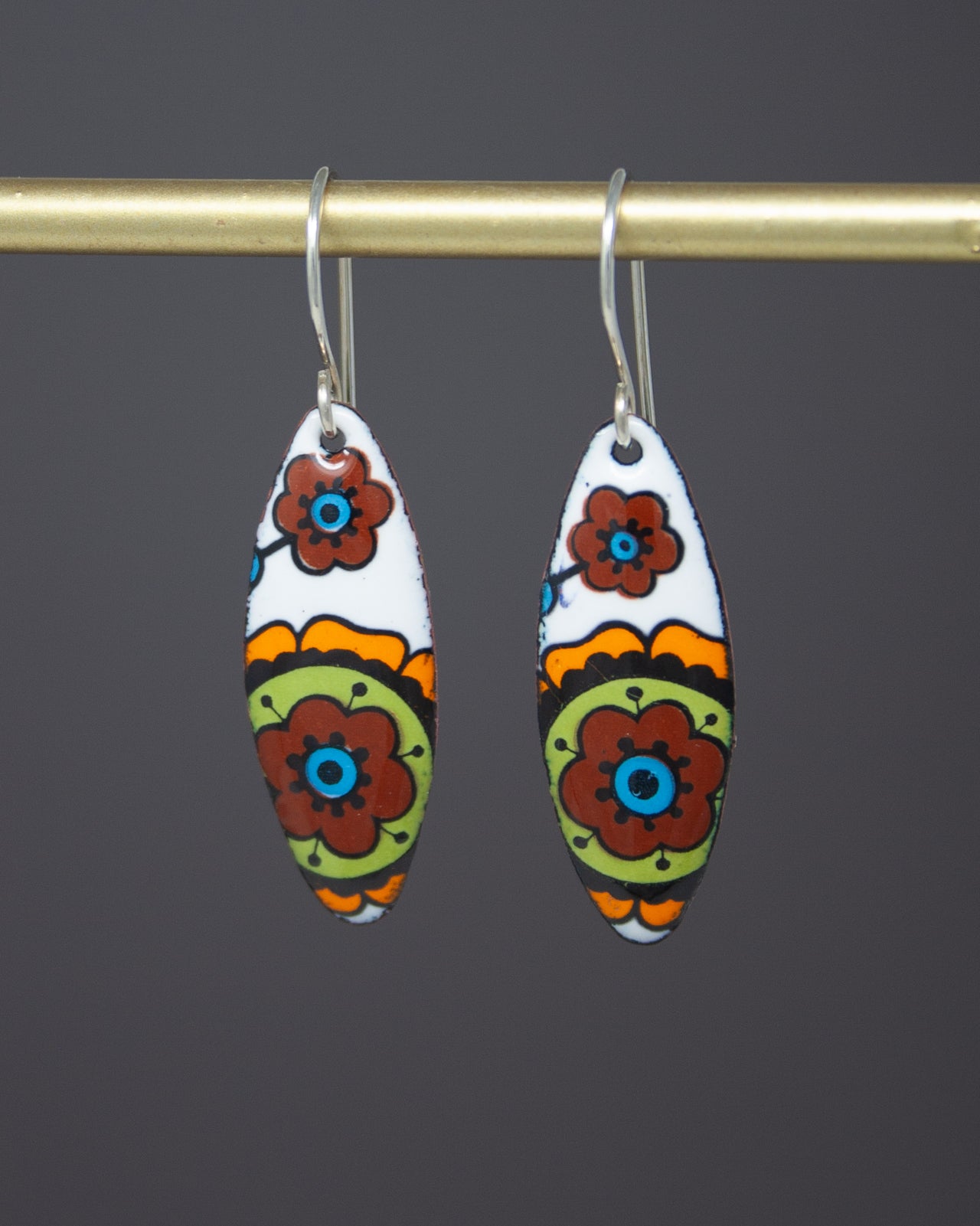 A pair of colorful earrings with floral designs hanging from a gold-colored metal hook.