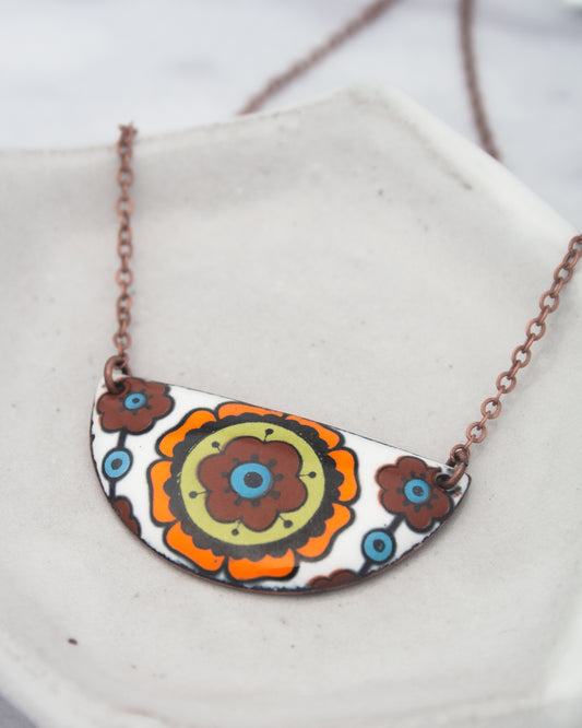 A colorful pendant necklace with a floral design on a white background.
