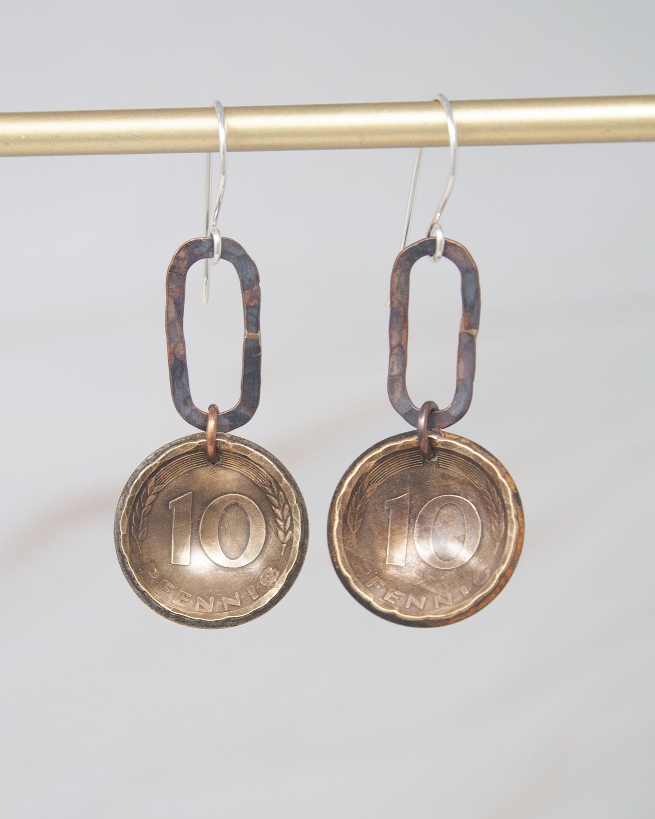 A pair of earrings made from two old coins, with the number 10 visible on both.