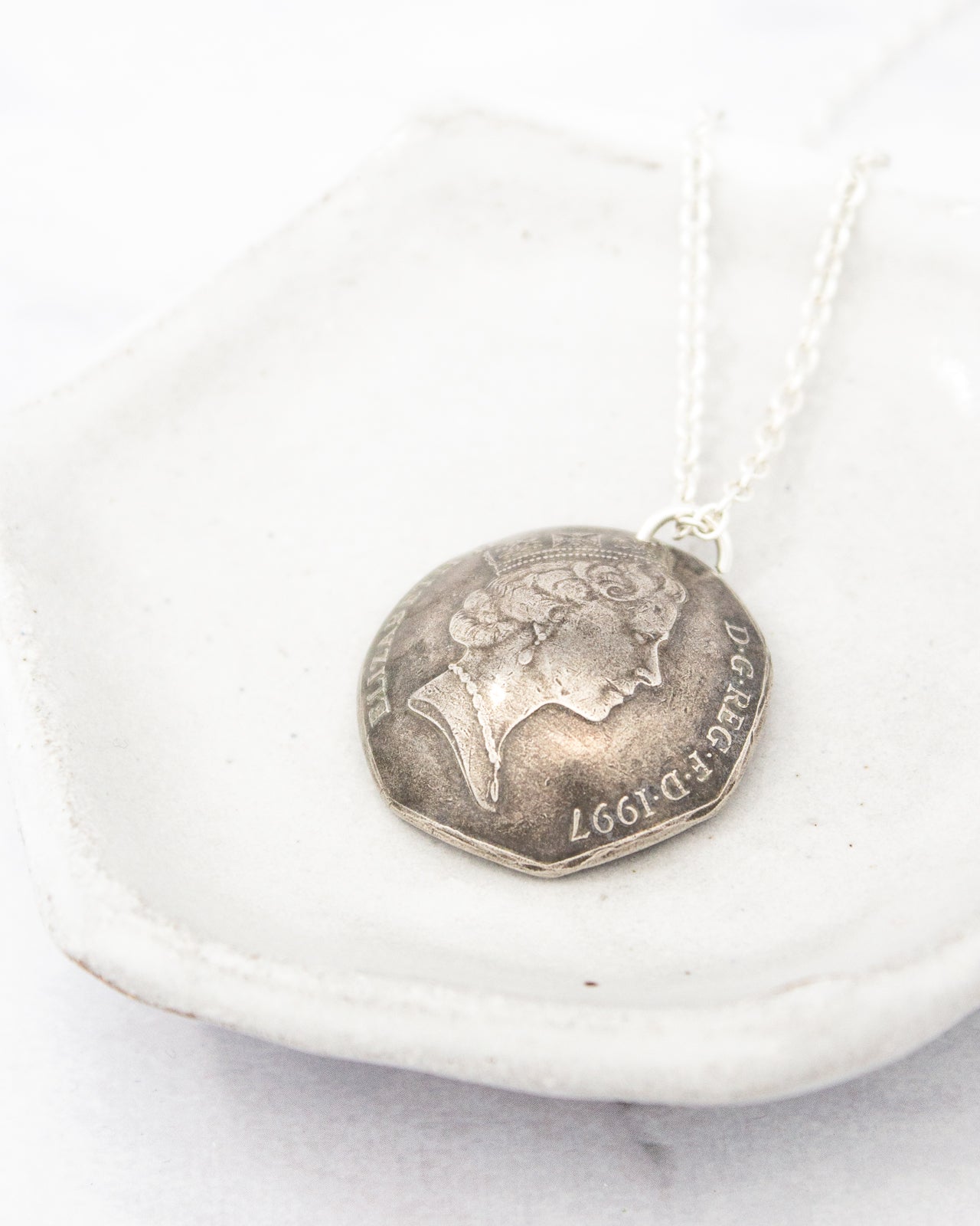 A silver-colored pendant necklace with a round medallion featuring a profile of a woman's face.