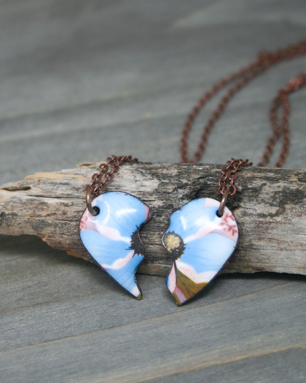 two broken heart shaped necklaces sitting on a piece of wood