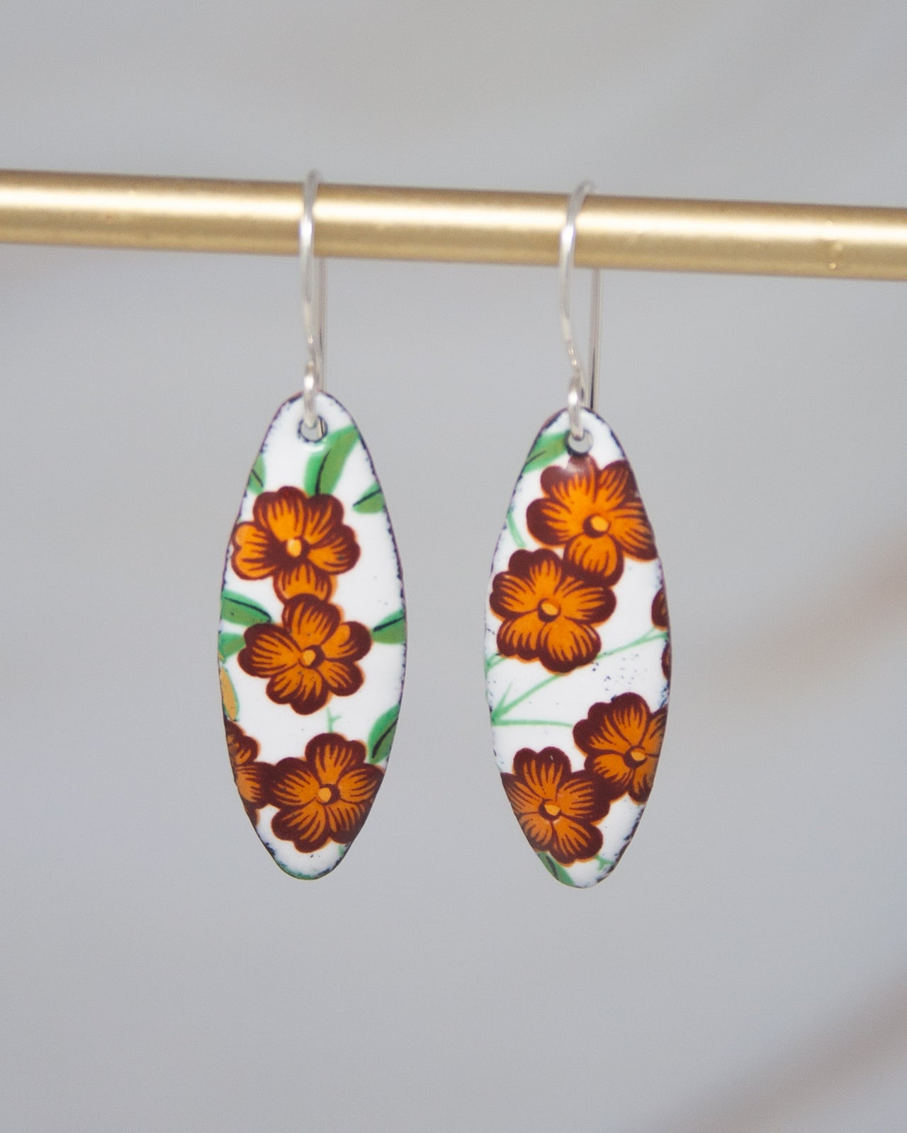 A pair of earrings with a floral design, featuring orange flowers on a white background.