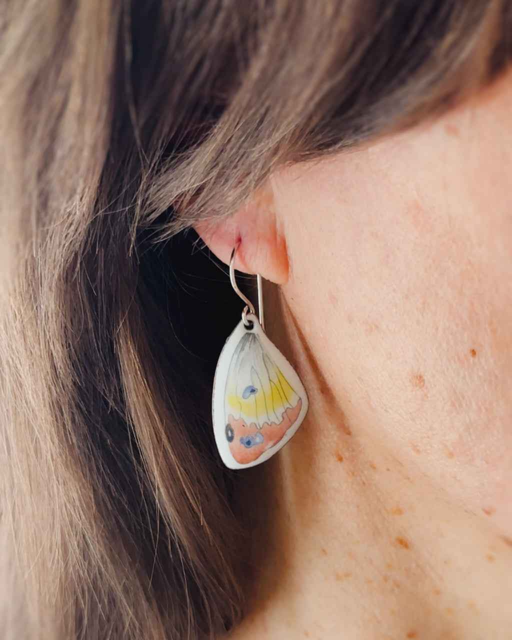 A close-up view of a person's ear wearing a pair of earrings with a butterfly design.