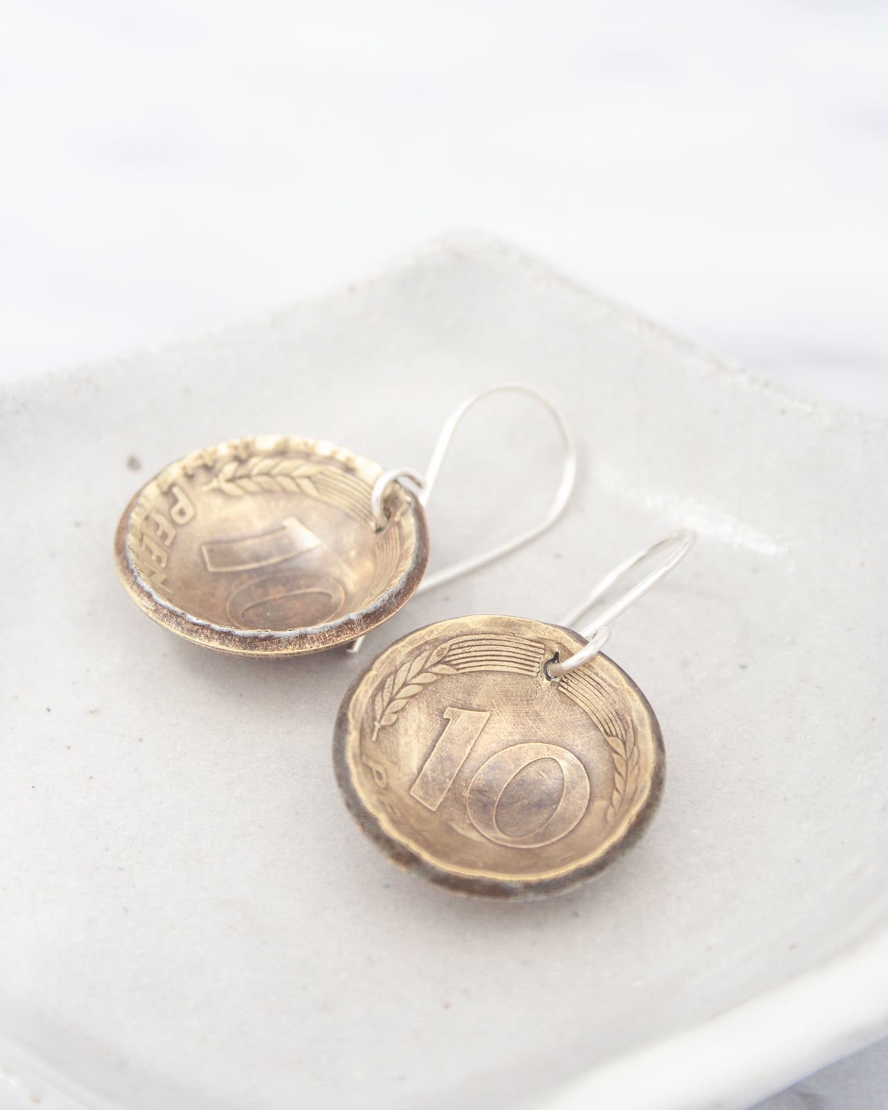 Two silver earrings with the number 10 on them, resting on a white surface.